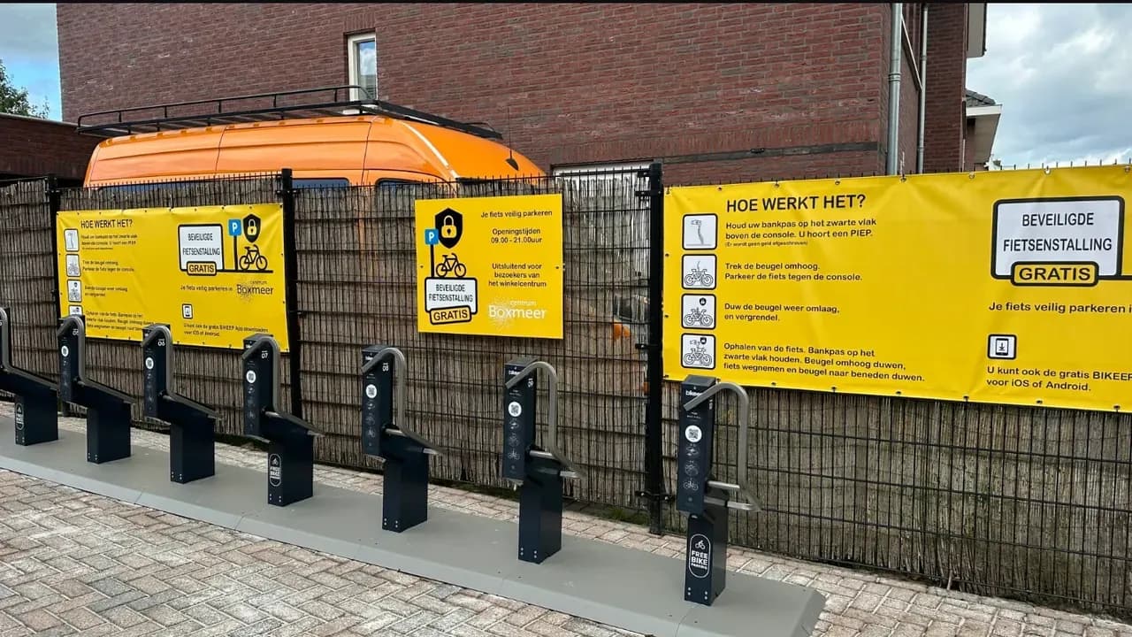 Ten black Bikeep smart bike docks under yellow how-it-works banners on Veerstraat in Boxmeer town center, the Netherlands