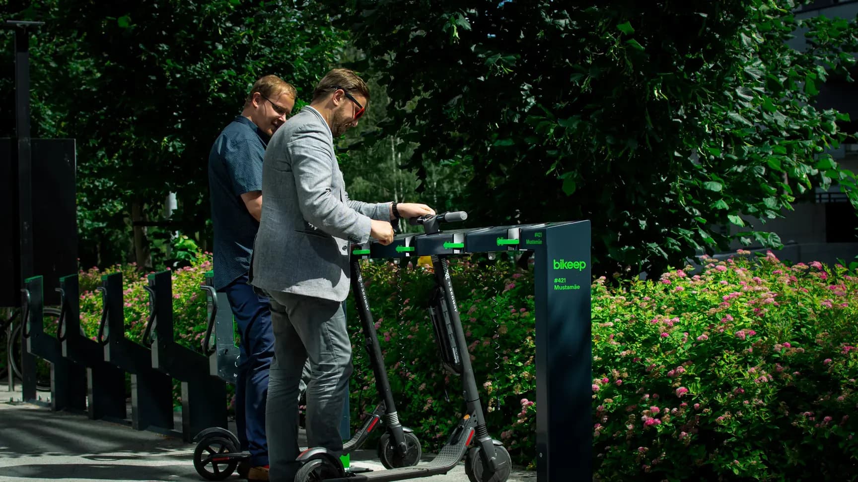 Two riders locking e-scooters into the Bikeep scooter parking station at Mustamäe keskus in Tallinn
