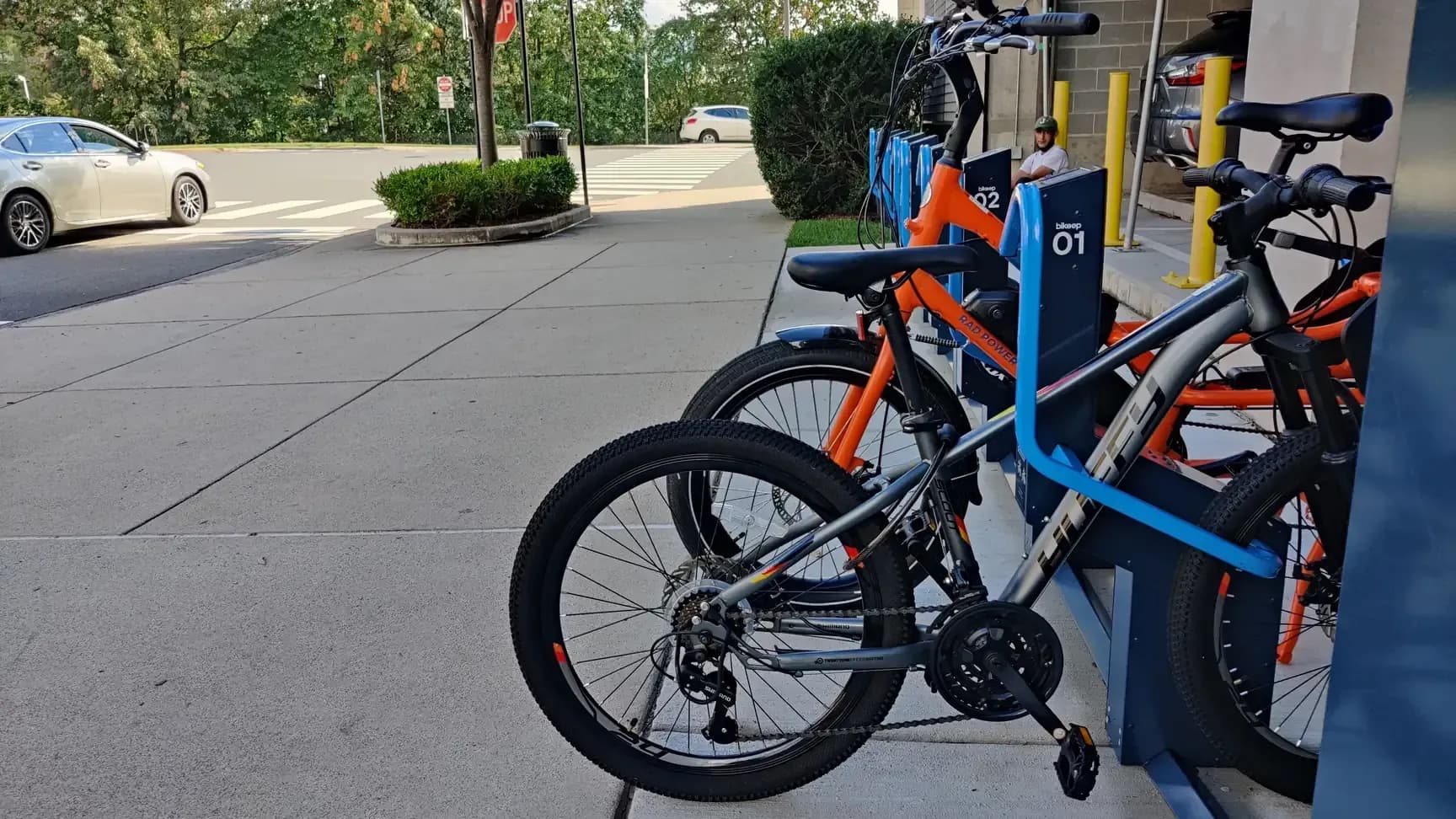 Bikeep smart bike parking station with an orange e-bike and a gray mountain bike locked in its docks outside a building