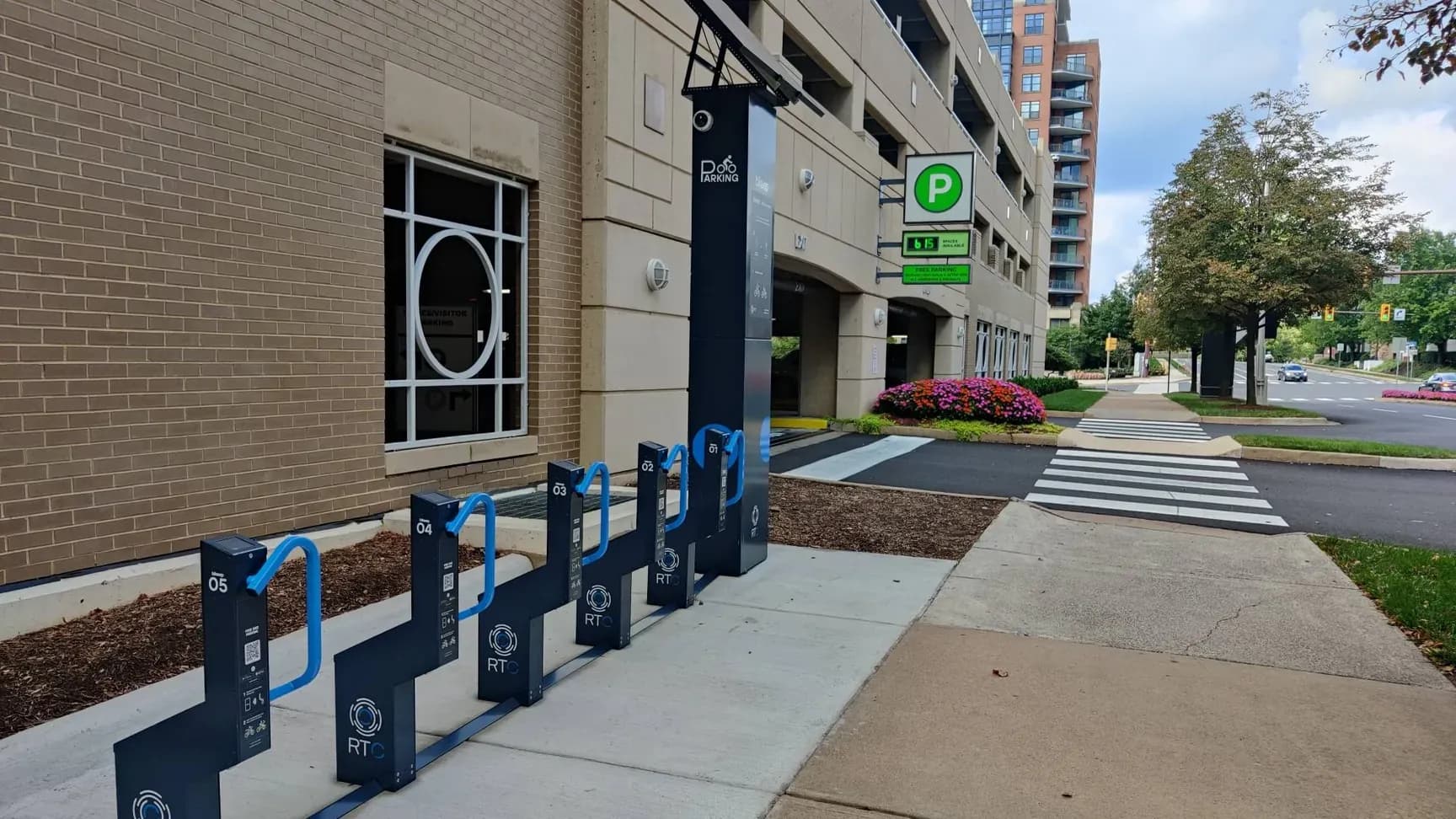A Reston Town Center branded Bikeep bike parking station with blue docks and a solar-powered column beside a parking garage in Reston, Virginia