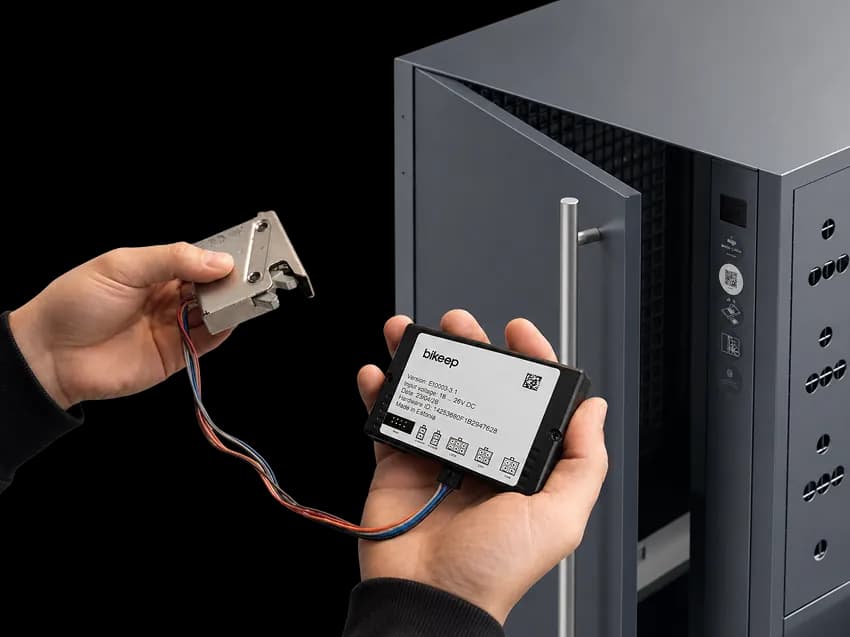 Bikeep IoT Smart Unit held in hand with bike locker in the background