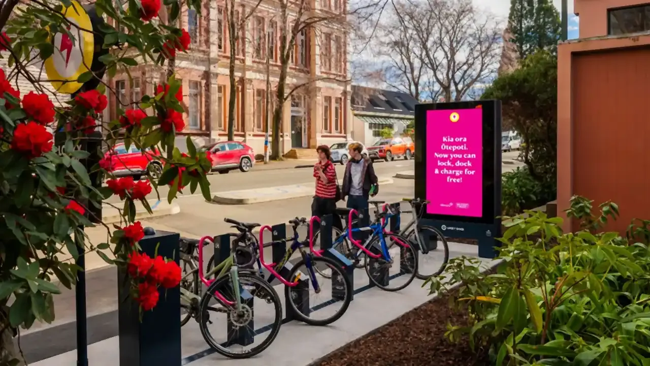 Bikes docked at a Locky Dock station in Dunedin beside a digital screen announcing free bike parking and charging