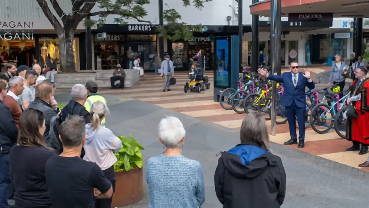 A speaker addresses a crowd at the launch of a Locky Dock bike parking station, with the mayor standing beside the docks