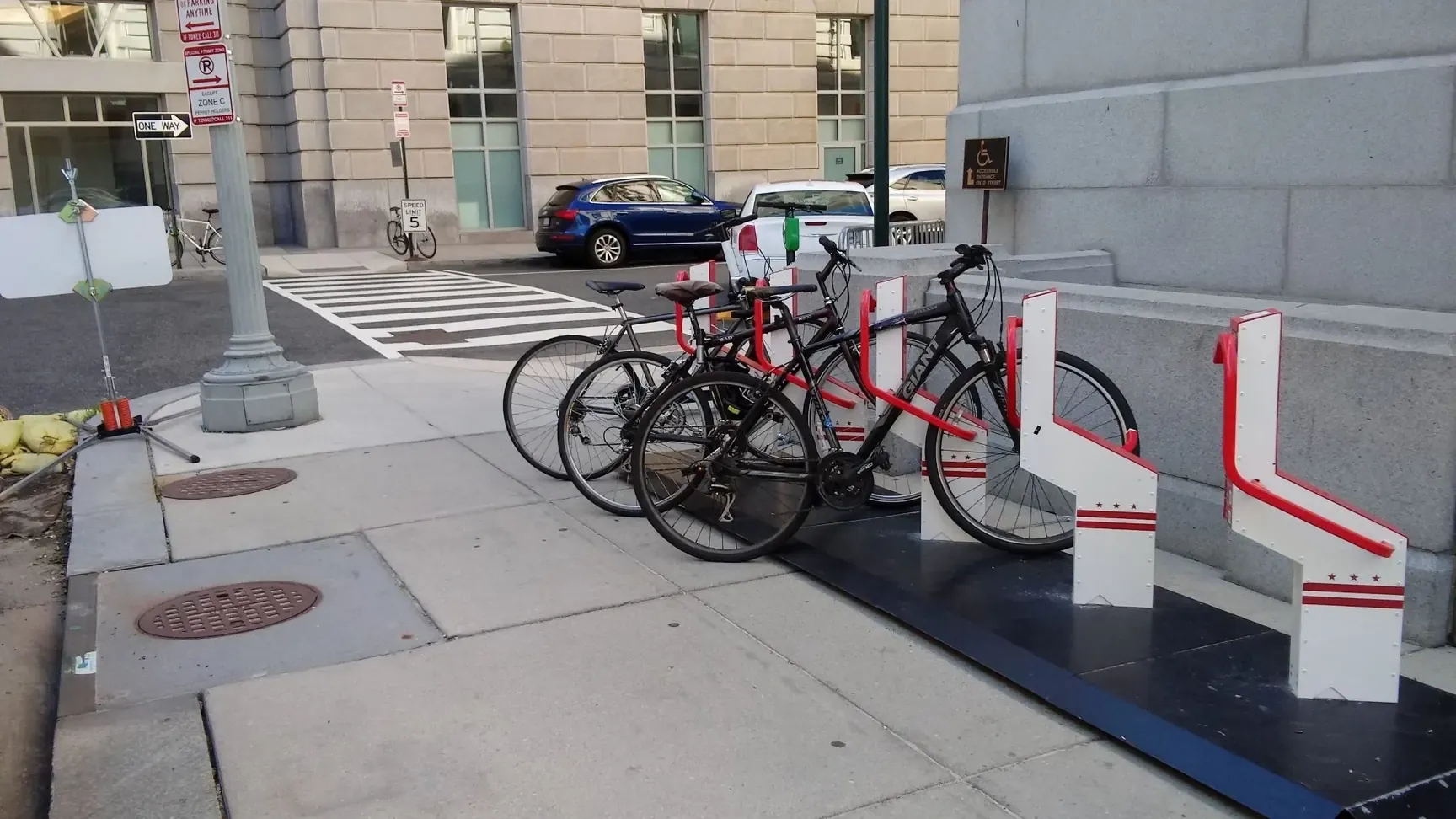 A Bikeep smart bike parking station with five docks in DC flag colours and bikes locked in, beside the Wilson Building in Washington, DC