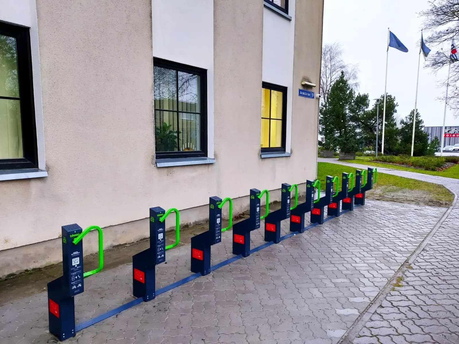 A 10-dock Bikeep smart bike parking station with green locking bars along the Rae Parish government building in Jüri